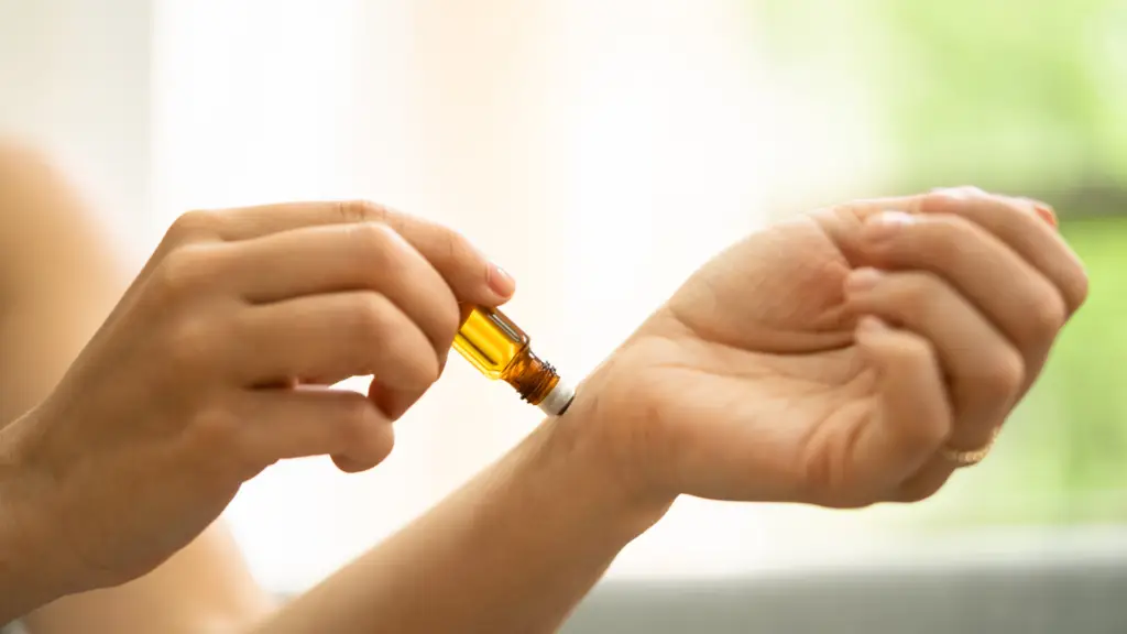 Close-up of a person applying essential oil from a small glass roller bottle to their wrist, with a soft, natural background out of focus.