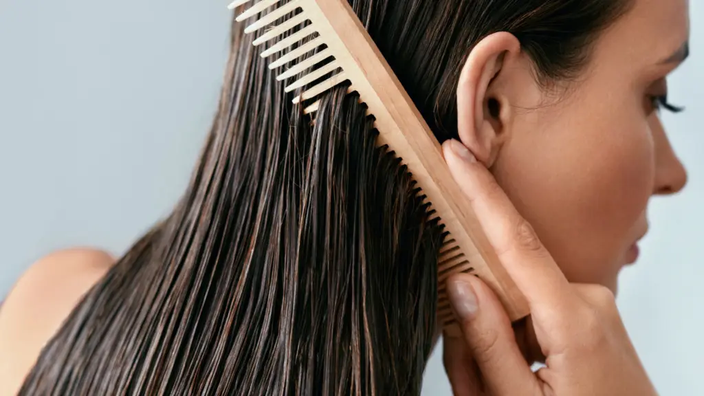 Close-up of a woman combing her wet, dark hair with a wide-tooth wooden comb, focusing on the hair's smooth texture and gentle grooming.