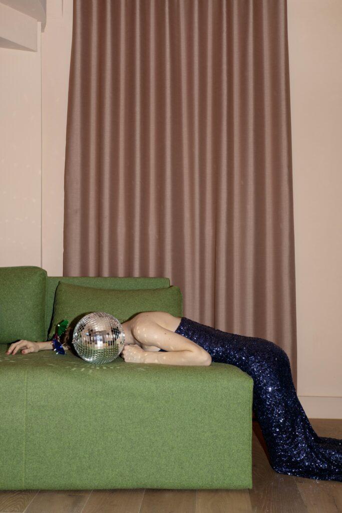 woman tired after a party, disco ball on green sofa